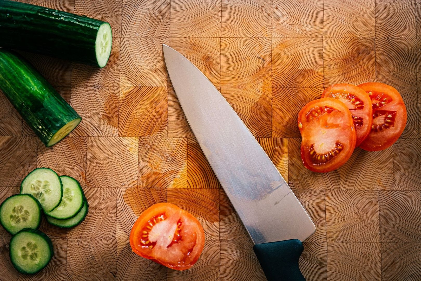 Kockkniv, gurka och tomater på en träskärbräda
